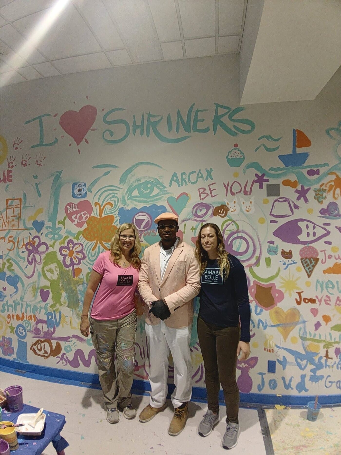 Three people in front of the seventh-floor playroom wall, covered in community drawings and handprints.